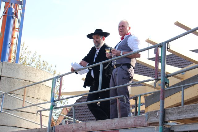 Zimmerermeister Ernst Schmidt (l.) beim Richtspruch auf dem Dach des Gemeindezentrums, (r.) Bauunternehmer Rolf Geist)