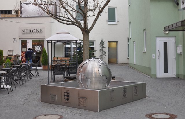 "Globus mundi 2006 - Unus alterum portat" steht auf Lateinisch an einer Seitenwand des Partnerschaftsbrunnens, was auf Deutsch heißt: "Weltkugel 2006 - Einer trägt andere." Im Sommer spendet der Brunnen den Gästen des benachbarten Cafés angenehme Kühle. Foto: ch