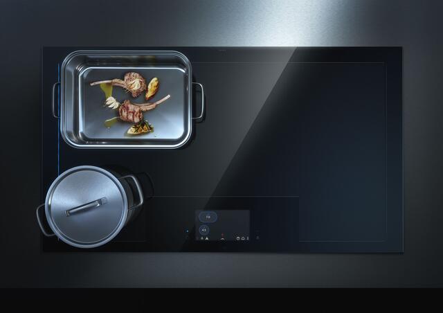 Prämiertes Premium-Ensemble: Der Design-Deckenlüfter mit individueller Höhenverstellbarkeit lässt sich mittels Fernbedienung, App- oder Sprache steuern und ermöglicht freie Sicht vor und nach dem Kochvorgang. Dazu ein smartes Vollflächen-Induktionskochfeld ohne vordefinierte Kochzonen. | Foto: AMK